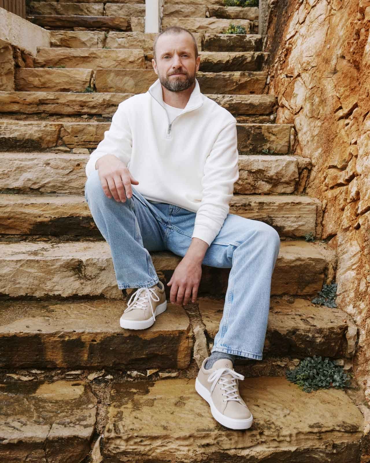 Man sitting on rock steps outdoors wearing casual sneakers