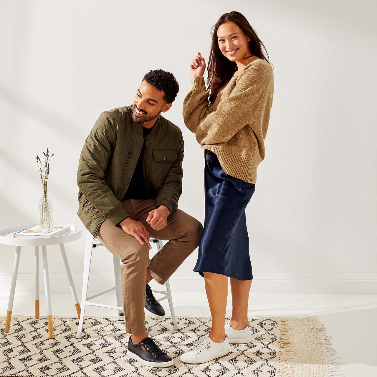 Man sitting on stool next to woman standing, both wearing casual sneakers