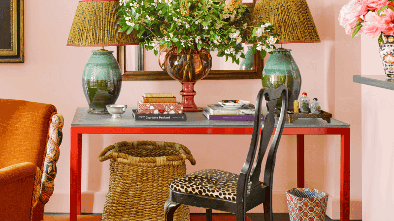 glass-top table with two lamps and a vase full of flowers in a room with light pink walls