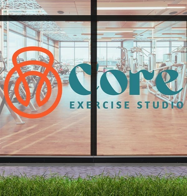 A glass window to the Core Exercise Studio bears its logo on a beautiful green and orange custom window graphic.