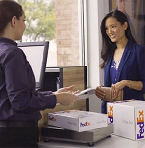 A happy customer smiles as she hands over her packages to a FedEx Office team members. 