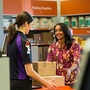 A smiling customer hands a FedEx team member two cardboard boxes for safe-keeping.