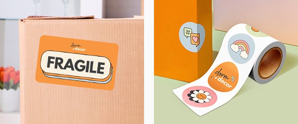 A custom orange sticker on a moving box reads, “FRAGILE.” A roll of colorful stickers sits unrolled on a table.