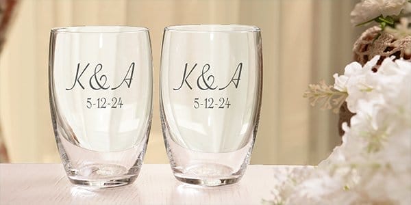 Two stemless wine glasses, personalized with the letters sit on a table and read 'K&A' with the wedding date.