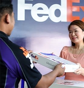 Woman handing package to professional FedEx Office team member.