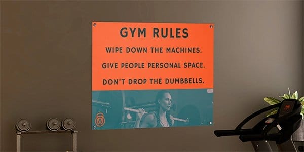 Branded orange metal wall sign hangs in a gym displaying rules and the 'Core' gym branding.