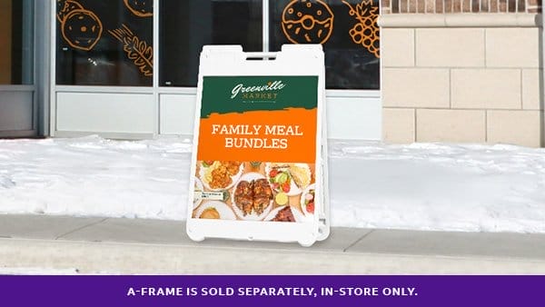 A green and orange a-frame sits outside of The Greenville Market that reads “FAMILY MEAL BUNDLES.”