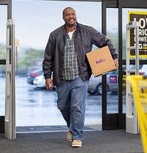 A happy customer arrives at FedEx Office with a package.