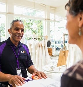 A smiling FedEx Office team member accepts a package from a customer.