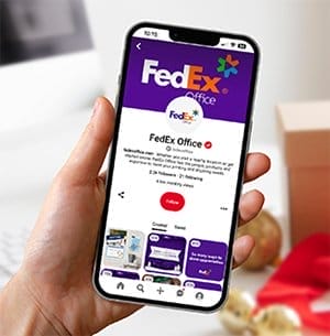 A hand holds a cellphone with the FedEx Office Pinterest page open on it.