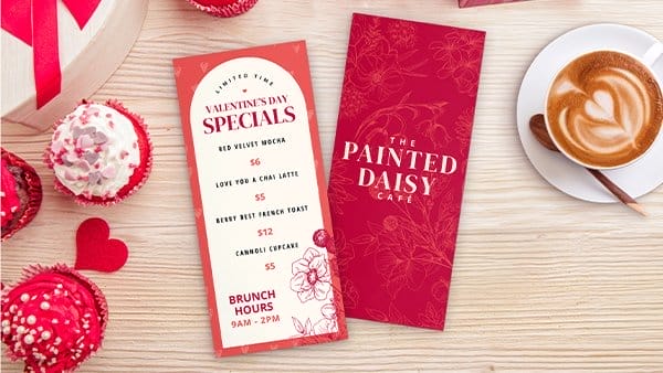 Two menus for The Painted Daisy sit on a table surrounded by cupcakes and coffee.