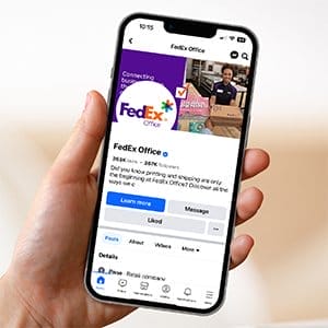 A hand holds a phone open to a FedEx Office social page. 