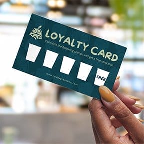 Hand holding a green loyalty card with 5 cups and a 'FREE' drink printed on it.