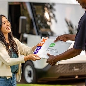 A happy woman receives her FedEx package from a FedEx team member.