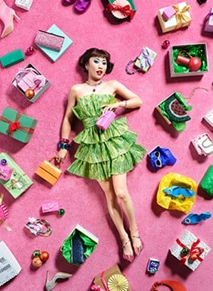 A woman in a green dress lays on a pink carpet surrounded by presents.