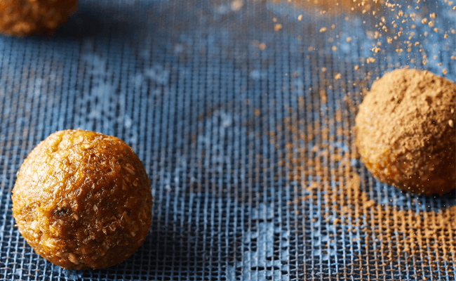 Two Mexican Chocolate Energy Bites coated with cocoa on a blue baking sheet