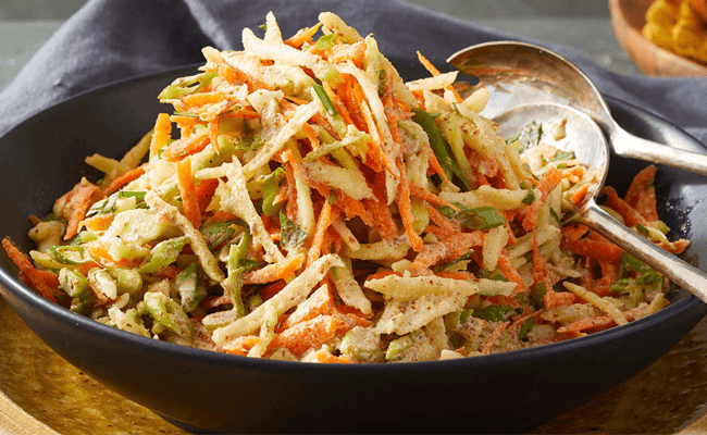 Best Broccoli Slaw in a black bowl with two silver serving spoons in the bowl