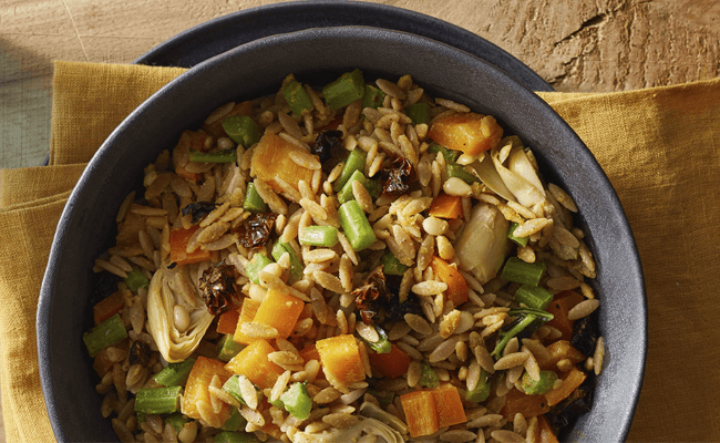 Orzo Salad with Kale Ribs in a black bowl on a yellow linen napkin