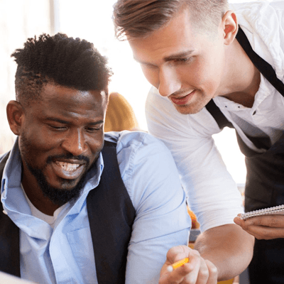 Man dining at a restauranttalking to a male server who is leaning over with a pencil and notepad, smiling