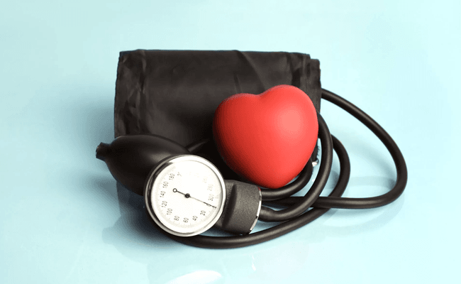 Blood pressure cuff with a red heart on top against a pale blue background