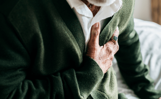 Close up of an older gentleman wearing a green cardigan, clutching his chest