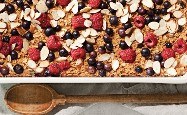 Oatmeal Breakfast Bake with Berries and Almonds in a white casserole dish next to a wooden spoon