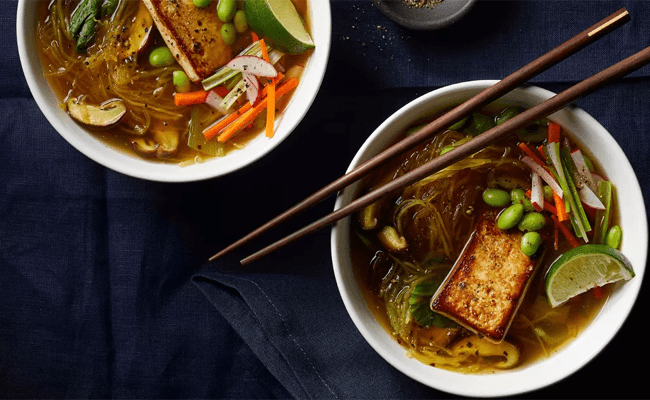 Two bowls of Spaghetti Squash Pho on a black background with a set of chopsticks sitting on the rim of one of the bowls