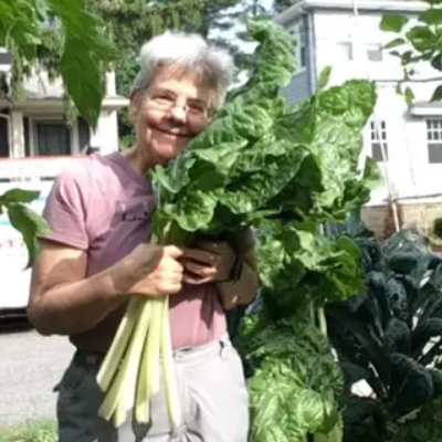 Karen Steiner holding a huge bunch of fresh-picked Swiss chard while smiling