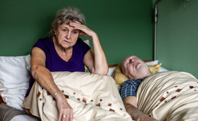 Senior woman sitting up in bed unable to sleep because her husband is snoring