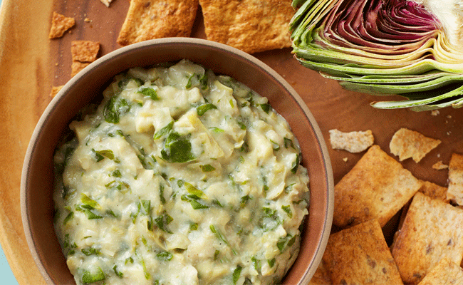 Vegan Spinach and Artichoke Dip on a wooden chopping board with crudités and half an artichoke