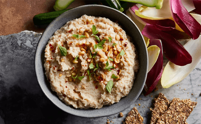 Roasted Cauliflower Hummus in a gray bowl surrounded by crackers and endive leaves