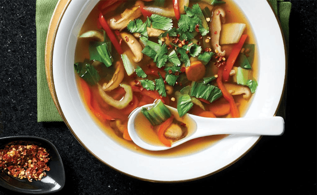 Sweet and Sour Vegetable Soup with a white Chinese soup spoon and a small dish of Sichuan pepper