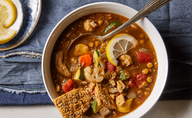 Clean-Your-Pantry Lentil-Vegetable Stew in a white bowl on a blue towel next to lemon slices