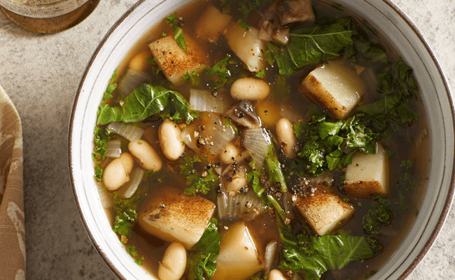 a bowl of minestrone with a thick broth, kale leaves, and chopped potatoes and white beans visible in soup