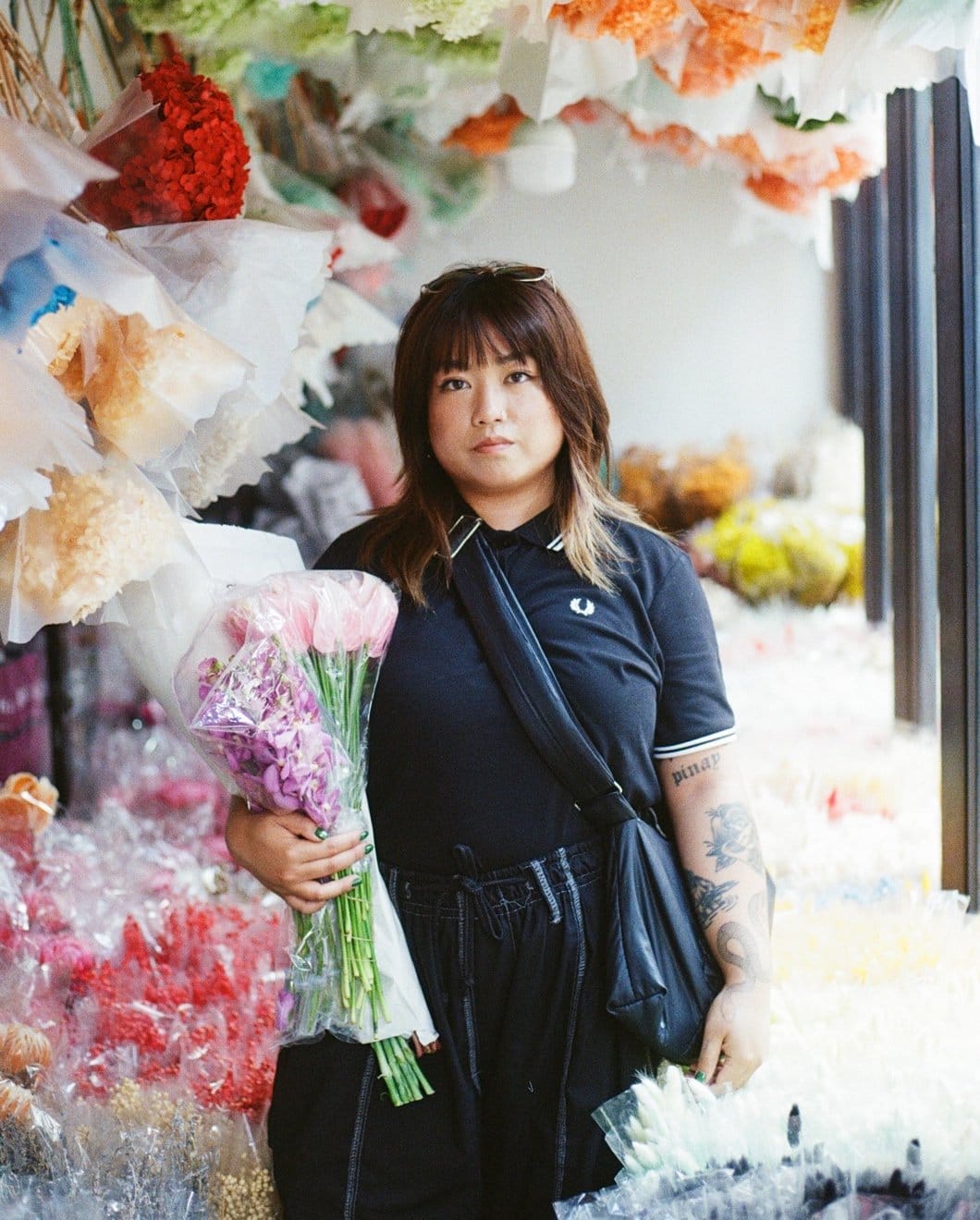 Asian female model wearing a black Fred Perry shirt in a flowers market.