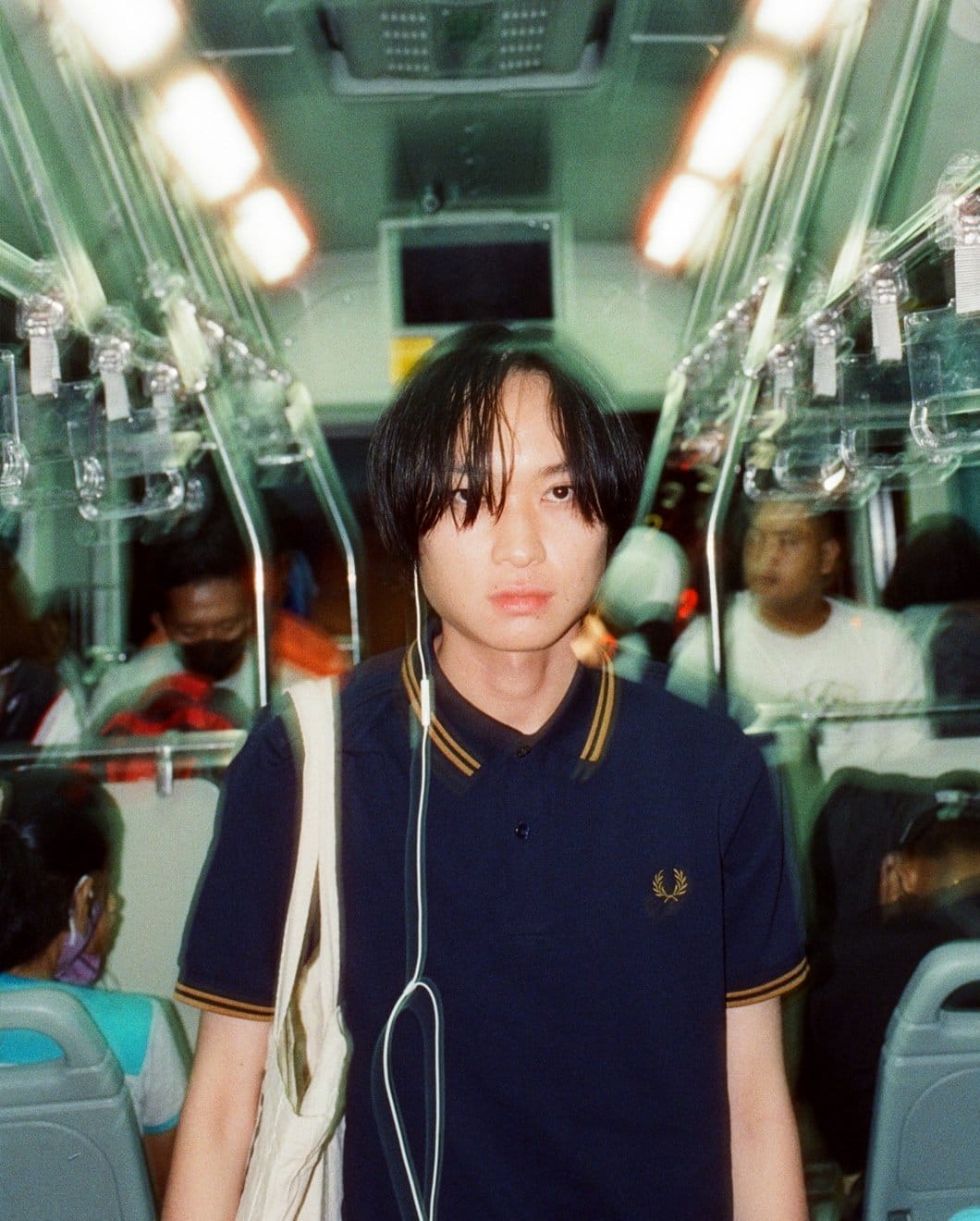 Asian male model wearing a navy, twin tipped Fred Perry shirt on the subway