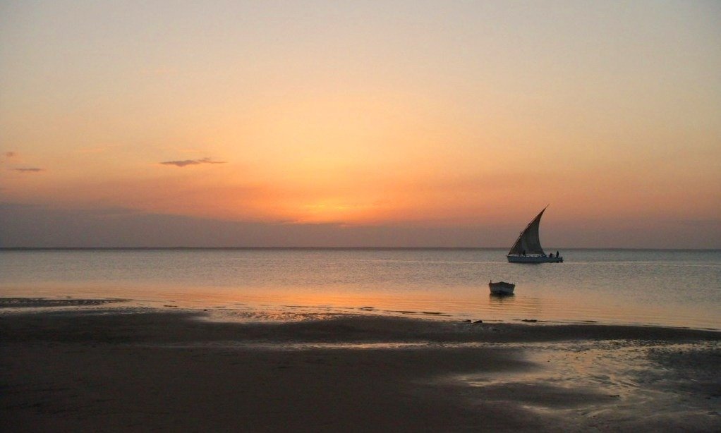 Boat sails past a beach at sunset