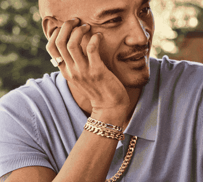 Male model wearing bold and chunky gold jewelry, including chain bracelets, necklace and diamond signet ring.