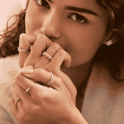 Model wearing stackable fashion rings, featuring dainty gold and diamond rings, diamond infinity bands, with diamond stud earrings to match.