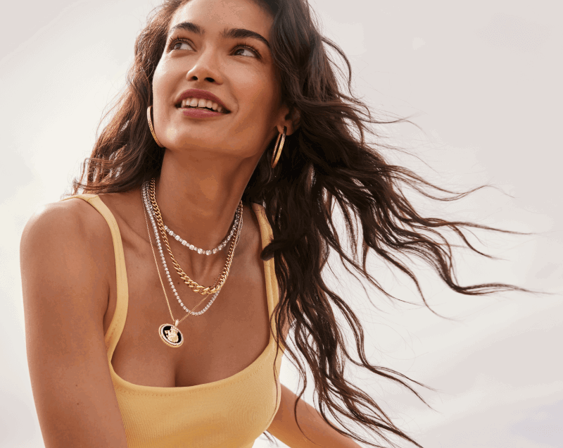 A smiling woman poses, adorned with a handful of stunning diamond & gold jewelry.