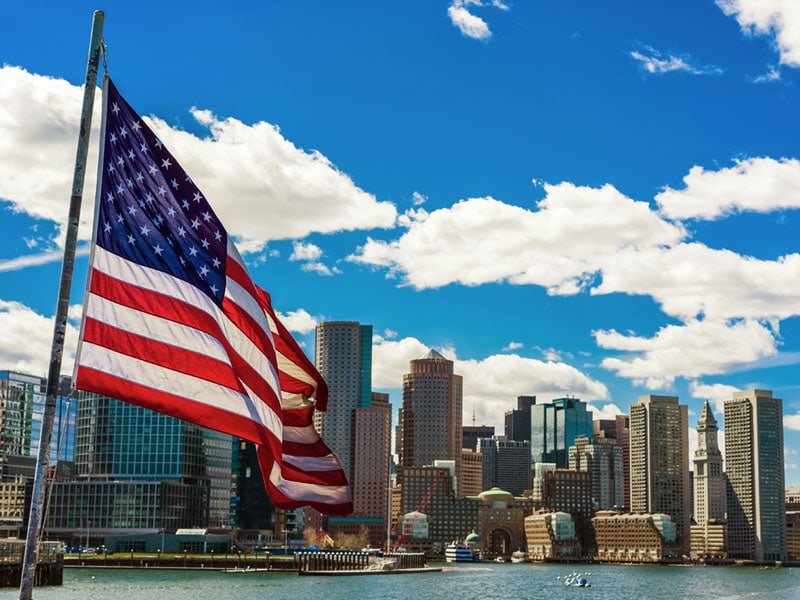 Boston skyline featuring iconic skyscrapers and landmarks, with the United States national flag in the foreground.