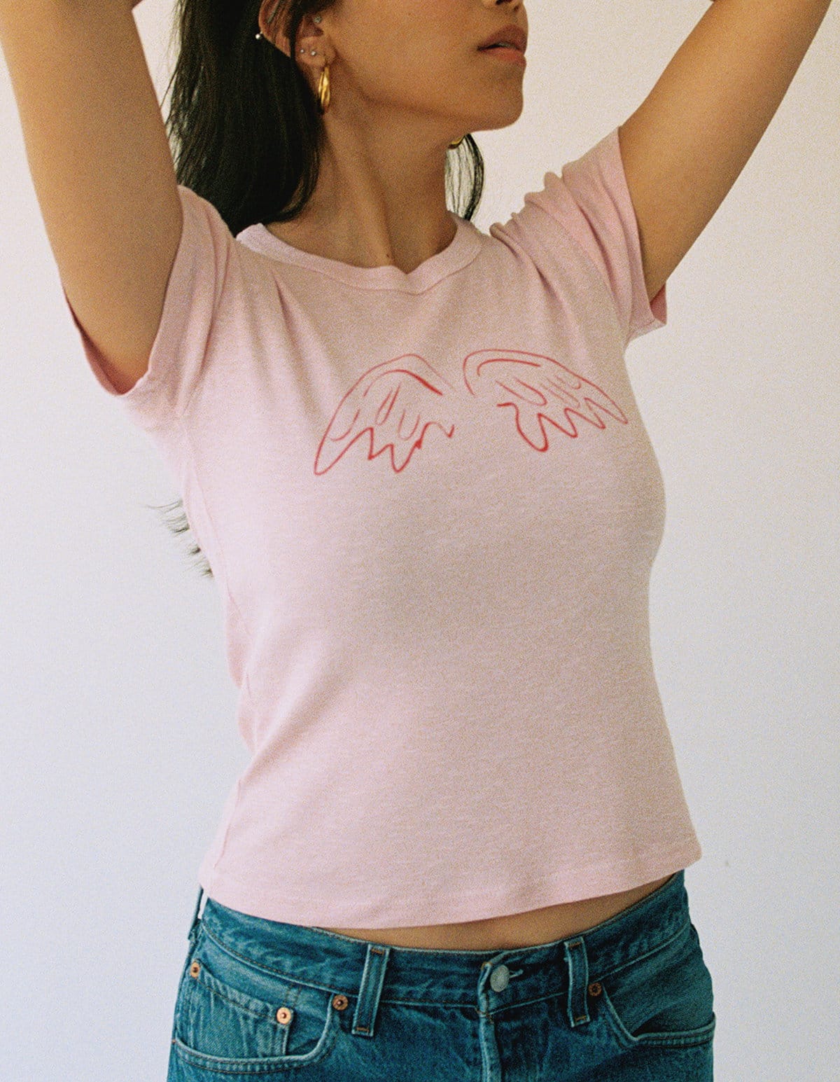 model wears a pink angel wing tee with jeans.