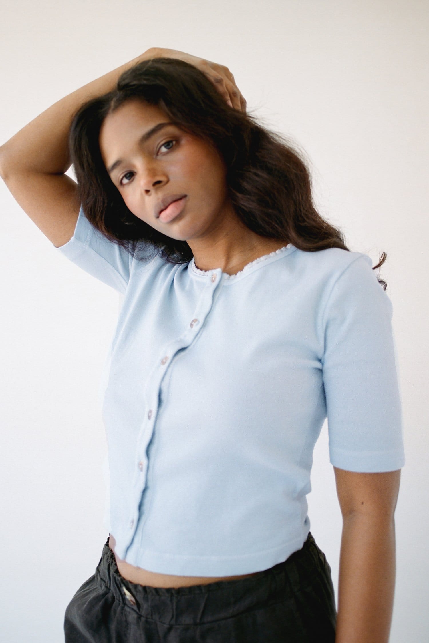 Model wears a pale yellow button up cotton top standing in a meadow.