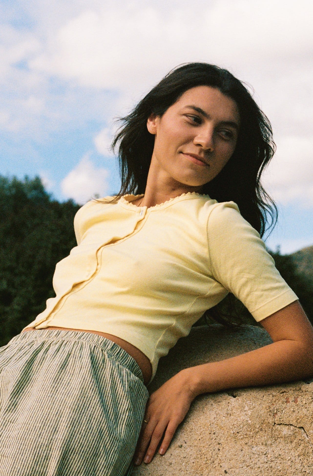 Model reclines on stone wearing a yellow cotton top.