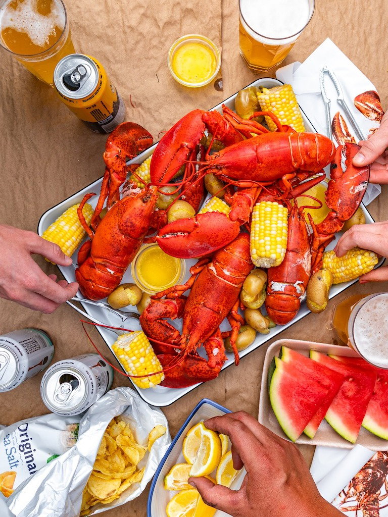 Hands reaching for food during a lobster bake