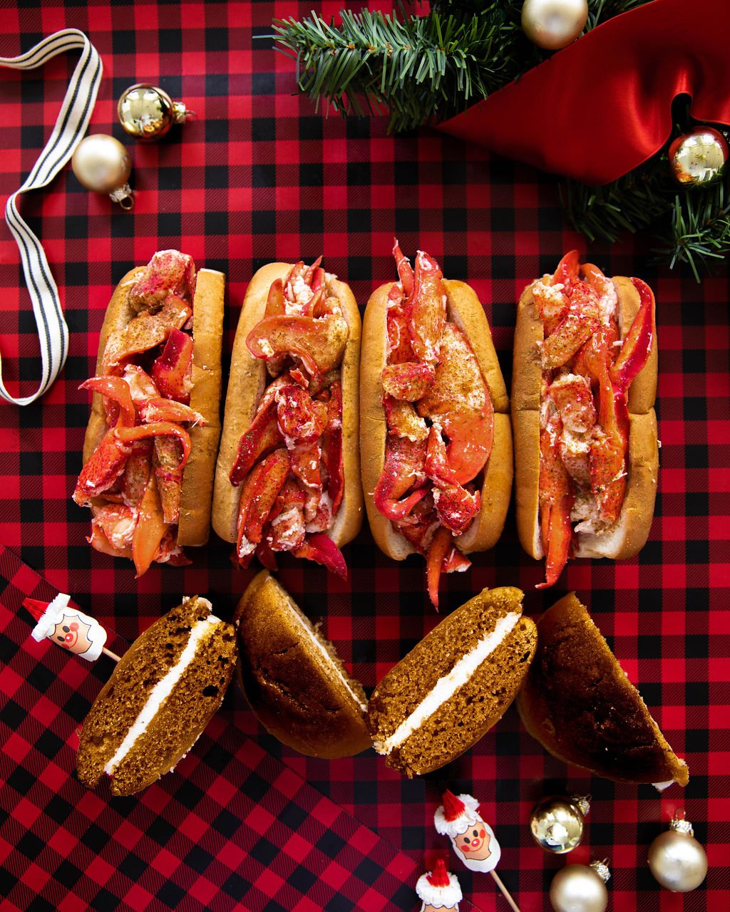 Four lobster rolls and whoopie pies cut in half on a holiday-themed table