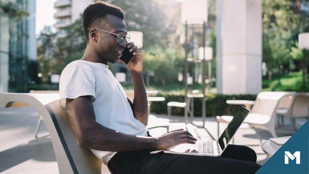 Man talking on the phone while scrolling on his laptop