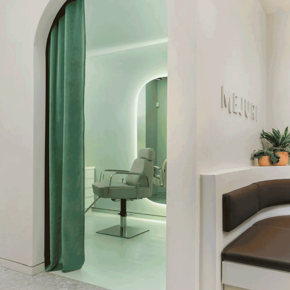A shot of a Mejuri piercing studio with a cream coloured chair placed behind a green velvet curtain. To the right of the studio is a waiting area with brown booth seating and the Mejuri logo printed on the wall.