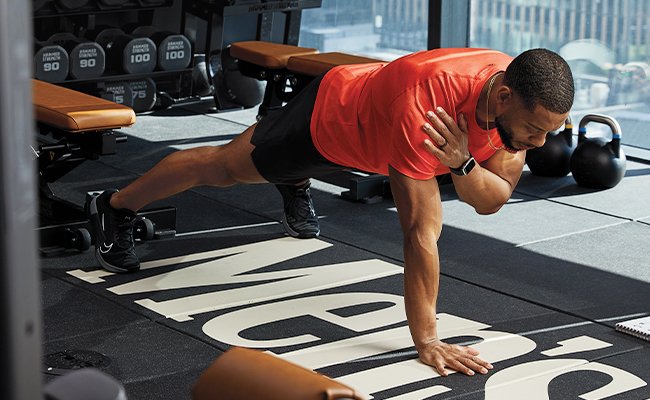 Man in gym reading doing one arm plank exercise