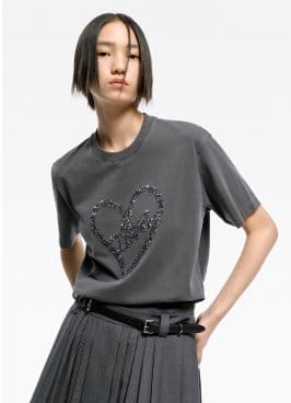 a model wearing a gray t shirt with a heart embroidered on it